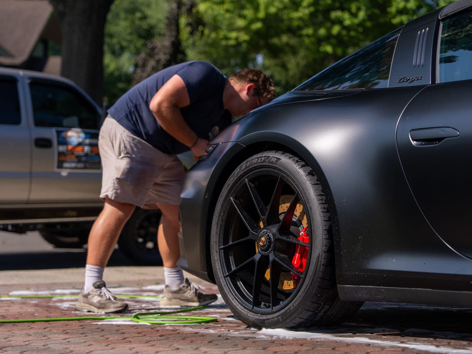Pro Performance owner-operator working the rocker panel of a matte-black Porsche 911, black wheel and red brake caliper in frame.