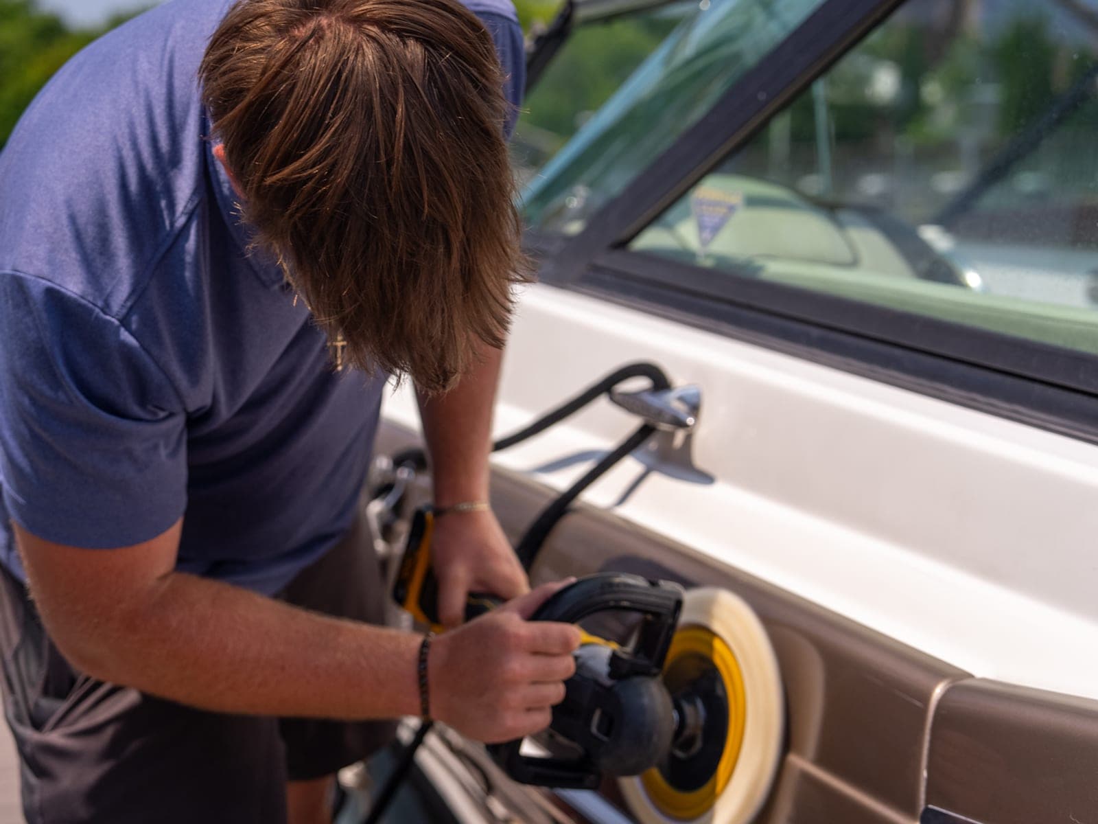 Pro Performance owner-operator running a dual-action machine polisher over a light fiberglass surface at a marina slip.