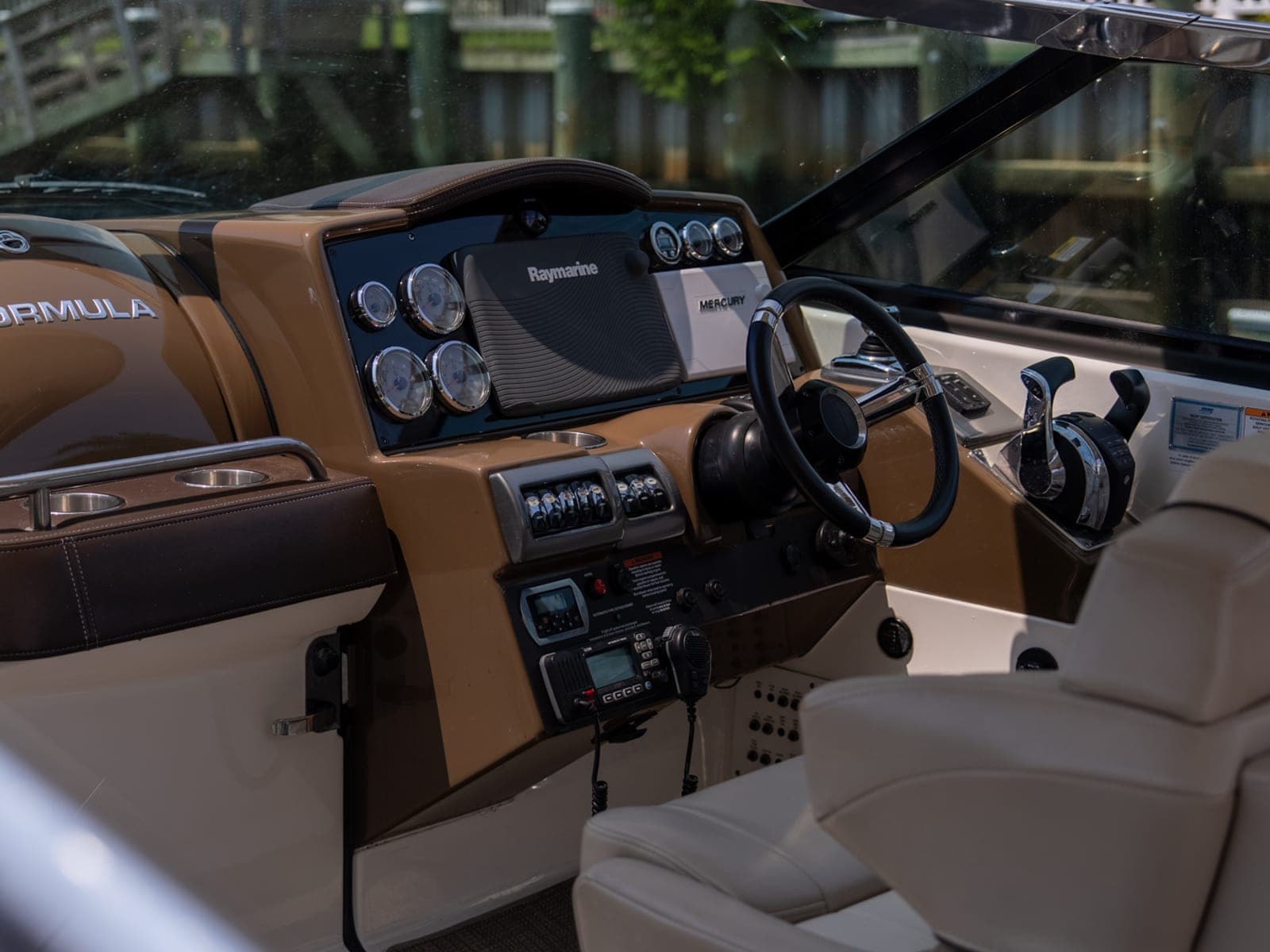Cockpit helm of a Formula cruiser at a marina slip: Raymarine chart plotter, chrome-rimmed gauges, Mercury throttle, cream and brown leather.