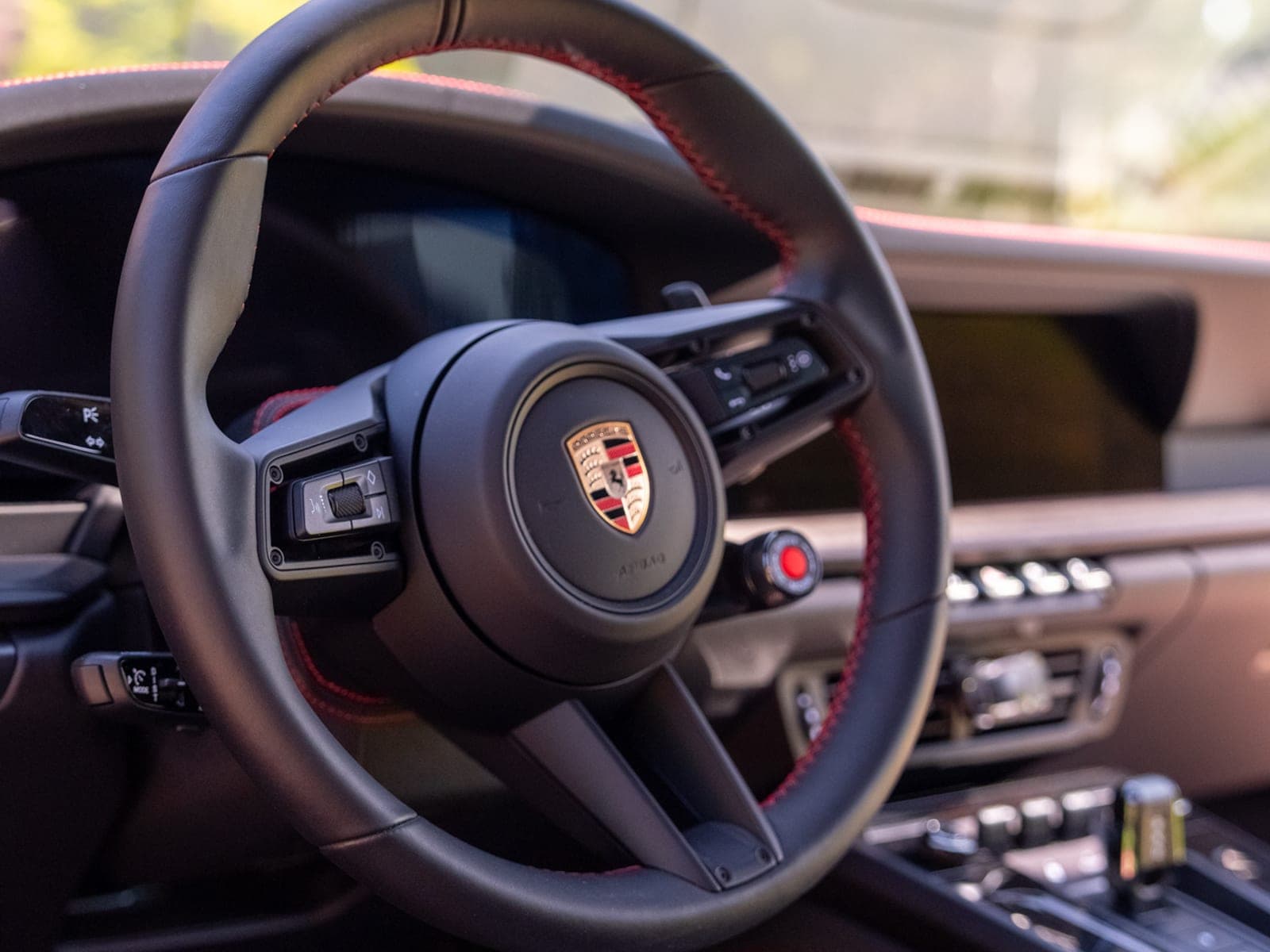 Close-up of a Porsche 911 GTS steering wheel and airbag boss, red-stitched leather rim visible, dashboard blurred behind, cleaned and conditioned.